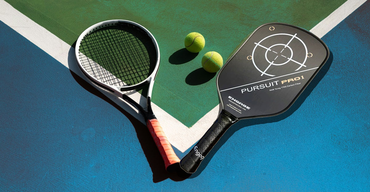 The Engage Pursuit Pro1 pickleball paddle lying on a pickleball court next to a tennis racket and tennis balls
