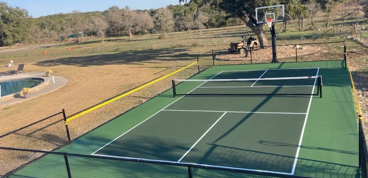 A backyard pickleball court with a basketball hoop behind